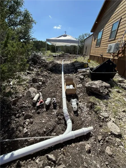 A pipe is being installed in the dirt in front of a house.