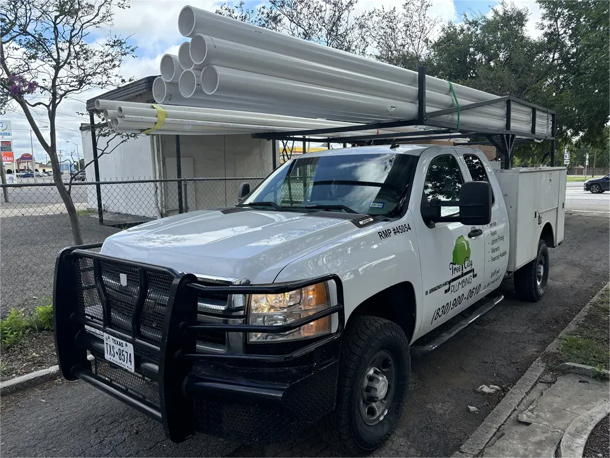 A white truck with pipes on top of it is parked on the side of the road.