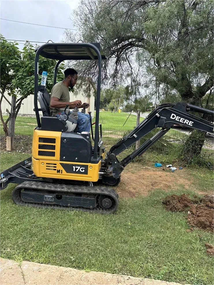 A man is driving a small excavator in a yard.