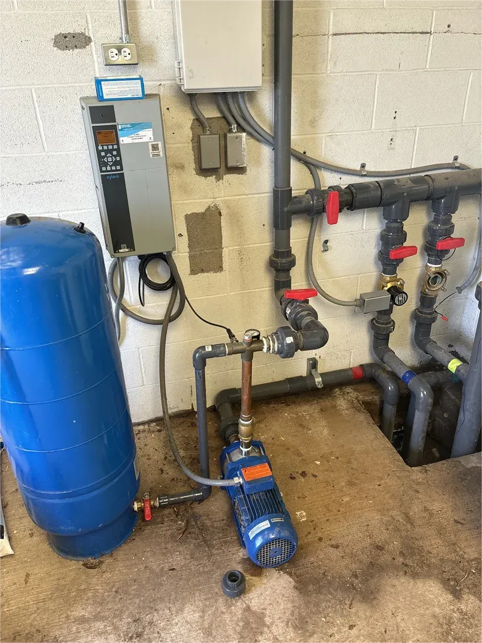 A water pump is sitting next to a blue tank in a room.
