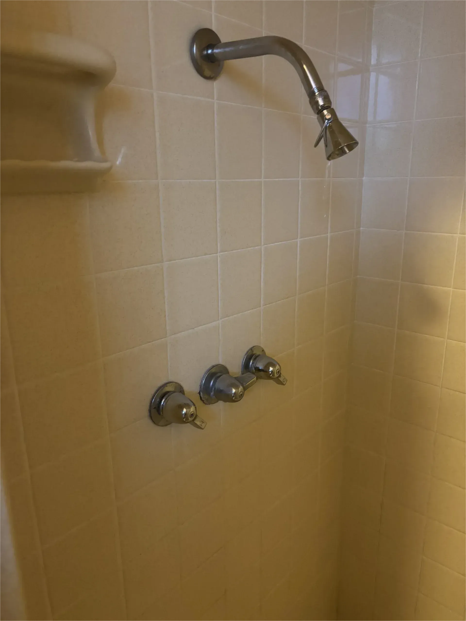 A shower with a shower head and three faucets on a tiled wall.