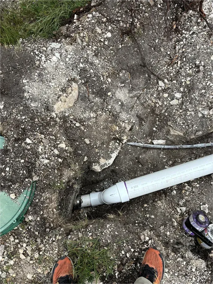 A person is standing next to a pipe in the dirt.