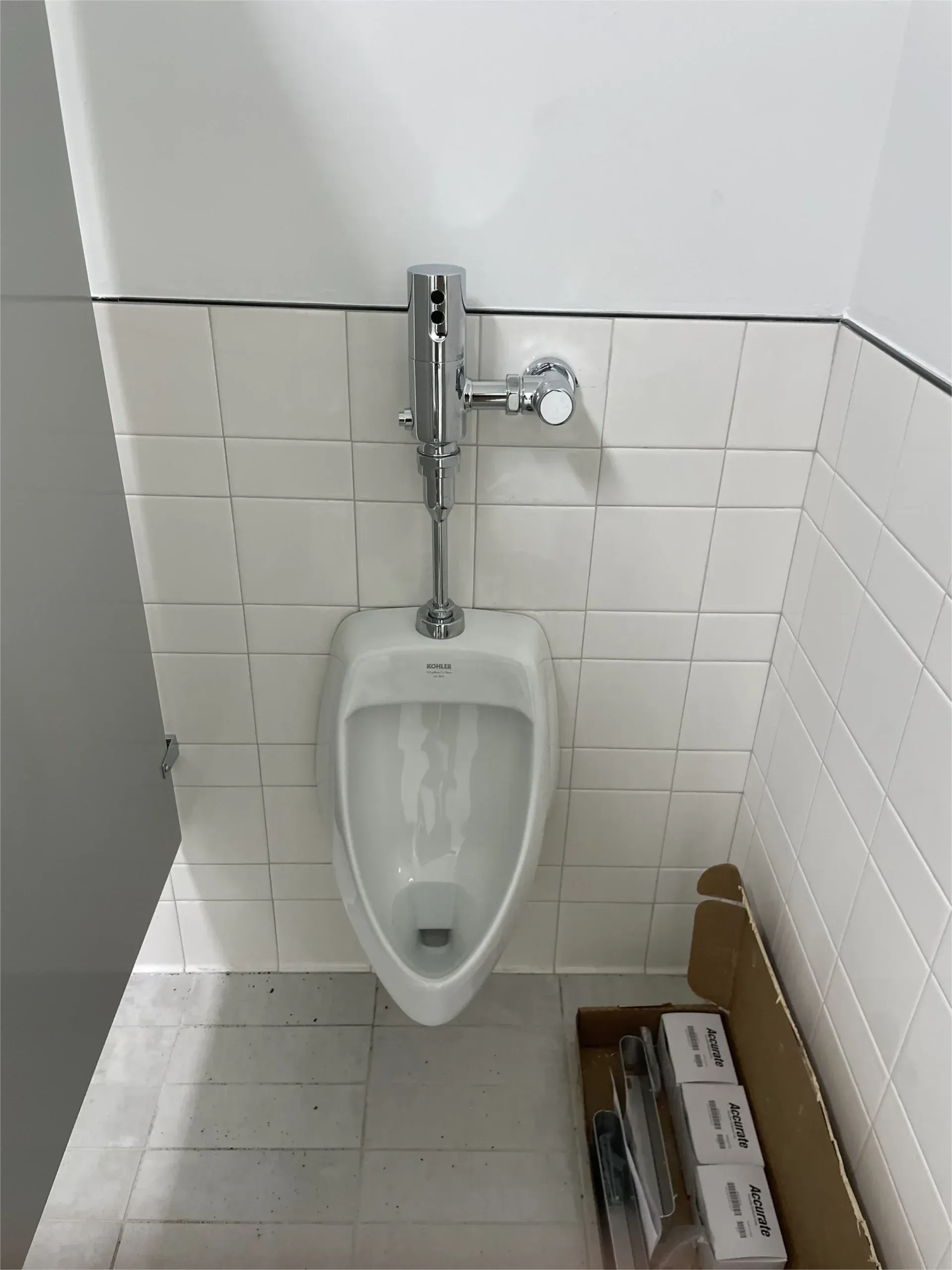 A urinal in a bathroom next to a box of toilet paper