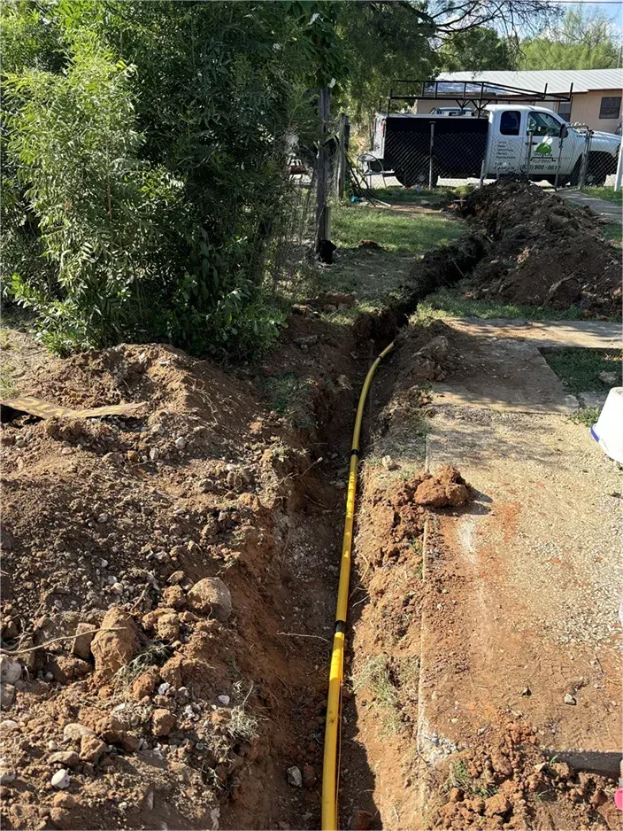 A yellow pipe is being installed in the dirt in a yard.