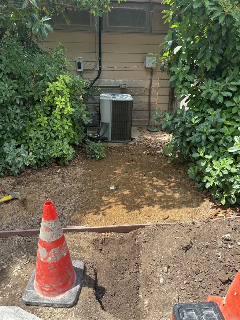 A red and white traffic cone is sitting in the dirt in front of a house.