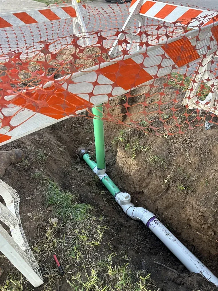 A green pipe is being installed in a hole in the ground.