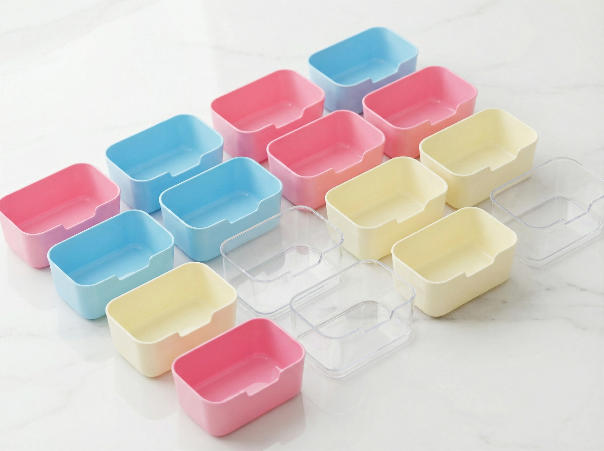 A collection of pastel-colored plastic storage bins in blue, pink, and yellow, with a few clear empty bins, on a white desk.