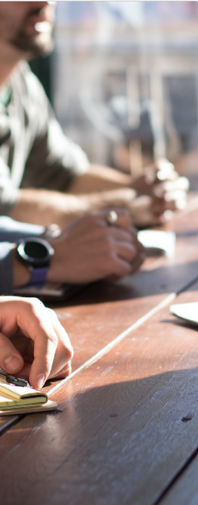 Des mains posées sur une table en bois, probablement lors d'une réunion, avec une personne portant une montre.