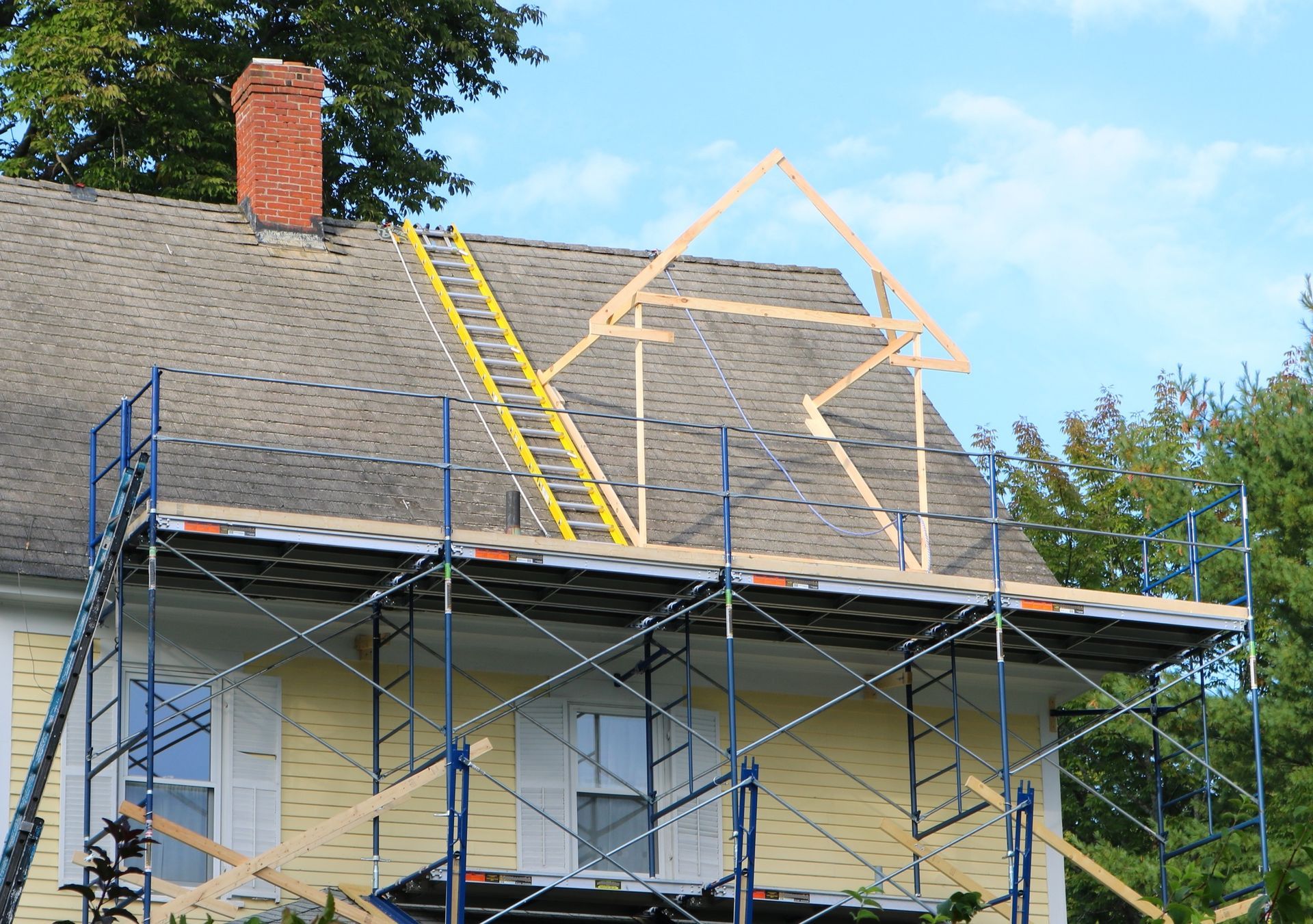 Roof under construction with scaffolding, ladders, and exposed framing on a house.