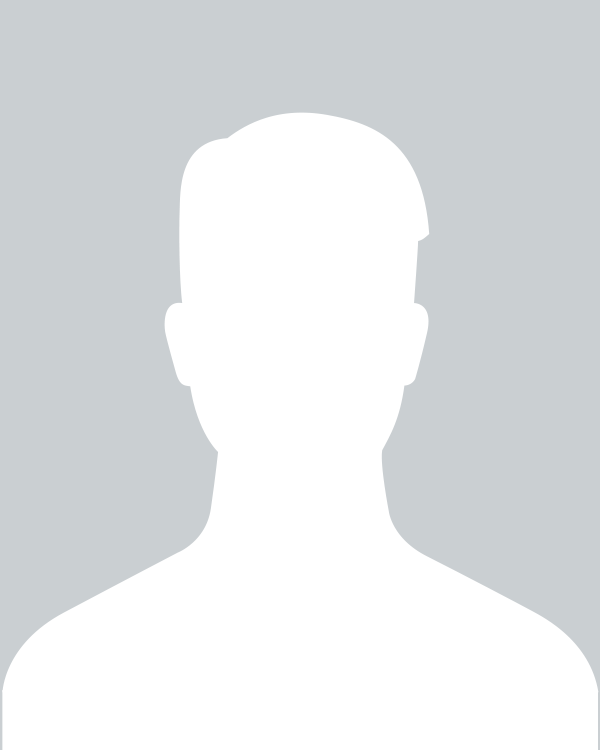 Woman with curly brown hair wearing glasses smiles at the camera, dark blue checkered shirt against black backdrop.