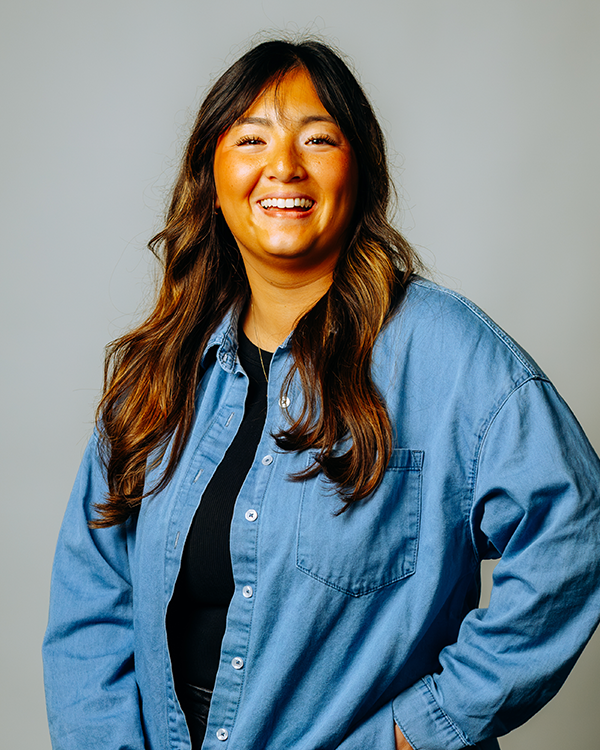 Woman in striped shirt smiles, hand on hip, against a gray background.