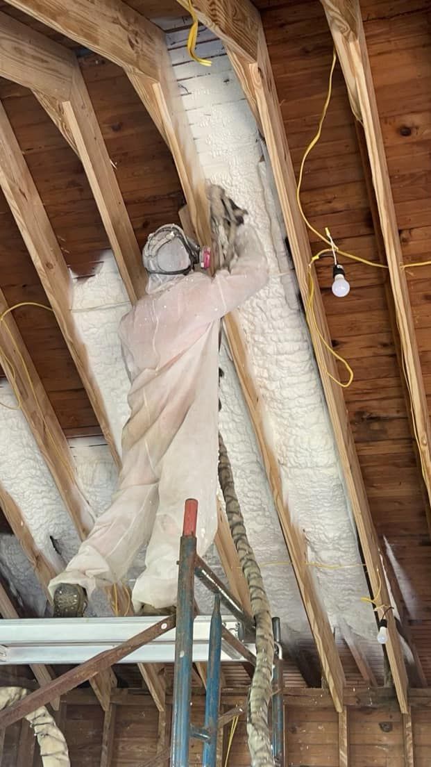 A man is spraying insulation on the ceiling of a building.