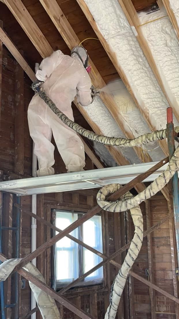 A man is spraying insulation on the ceiling of a house.