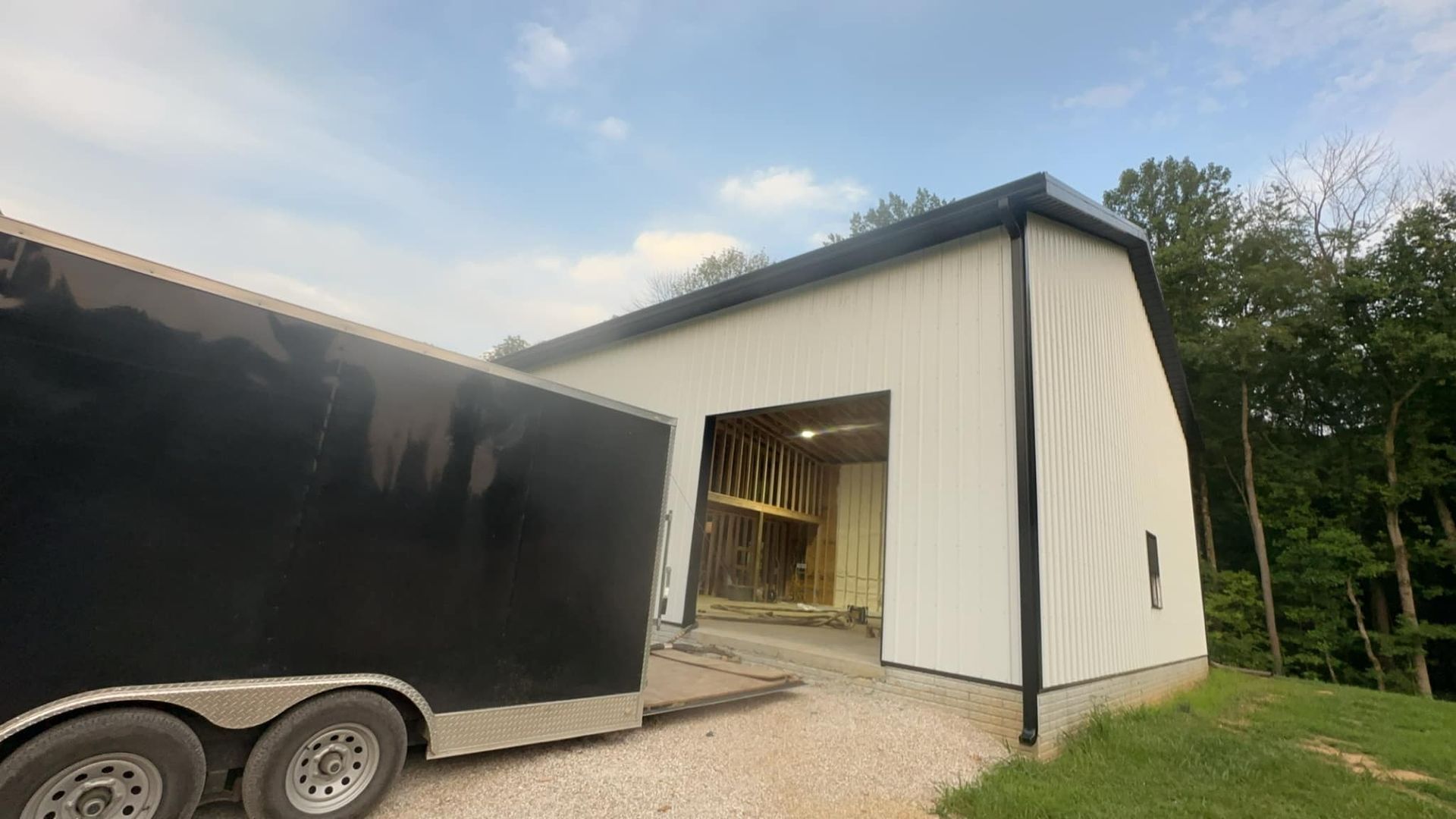 A black trailer is parked in front of a white barn.