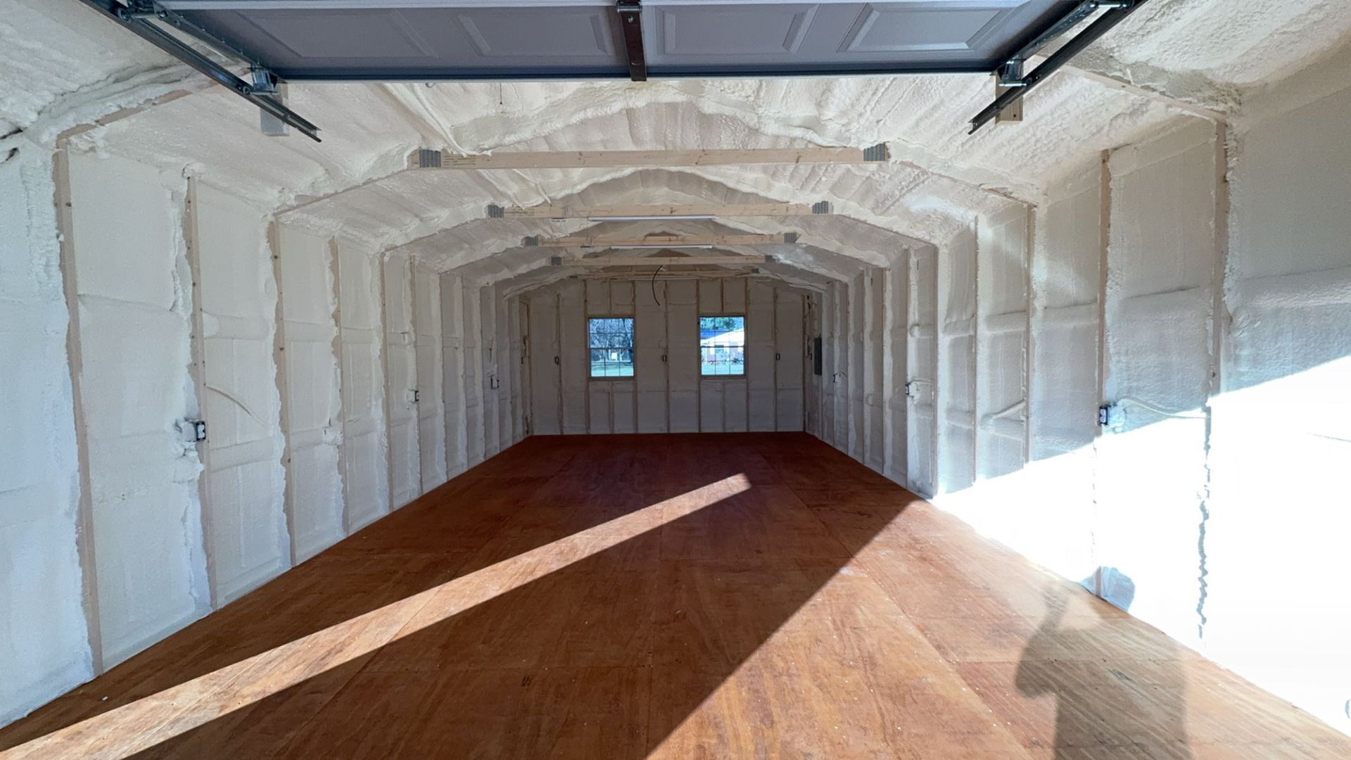 An empty garage with a garage door and a wooden floor.