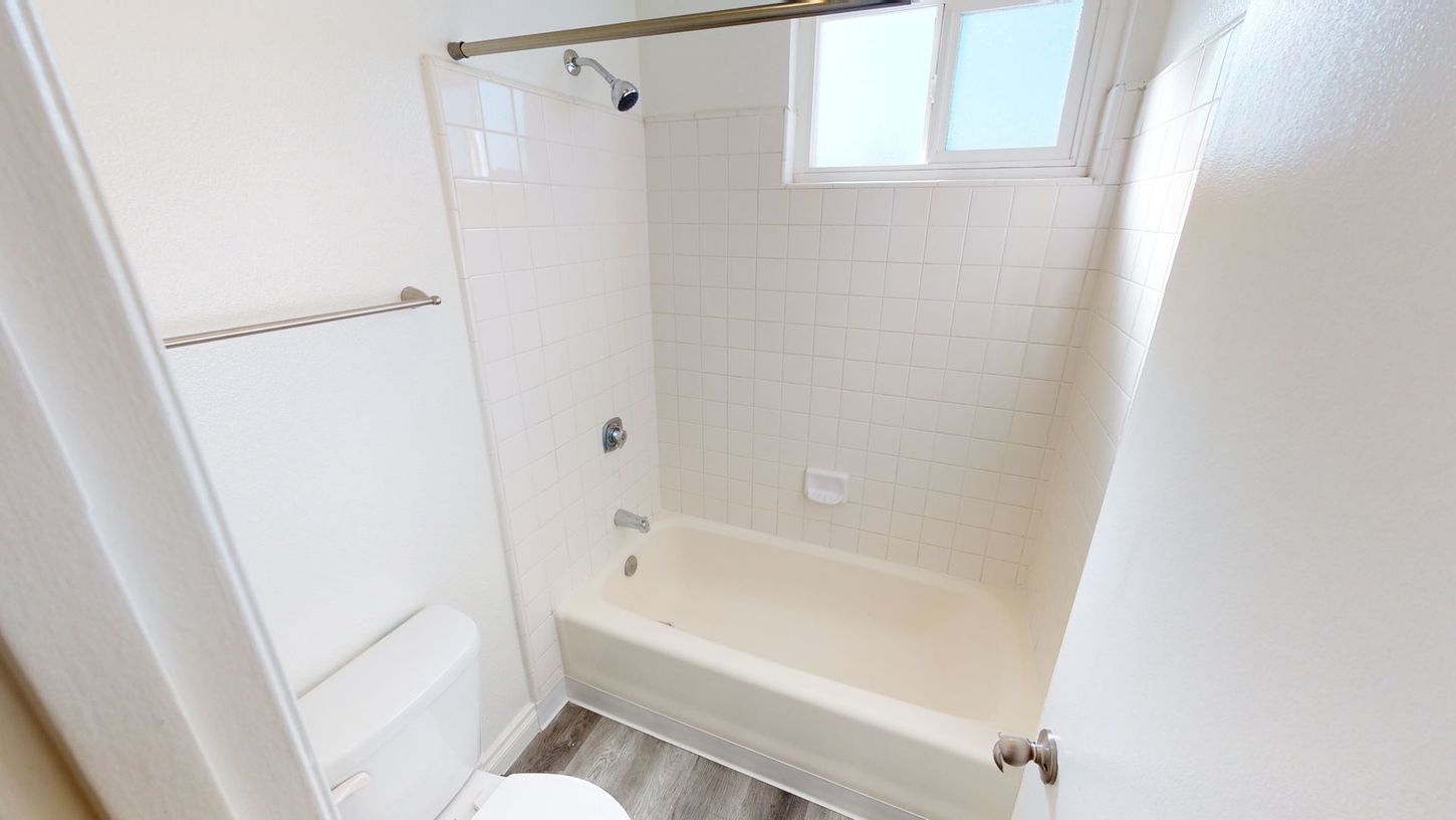 White bathroom with a bathtub, toilet, and window.