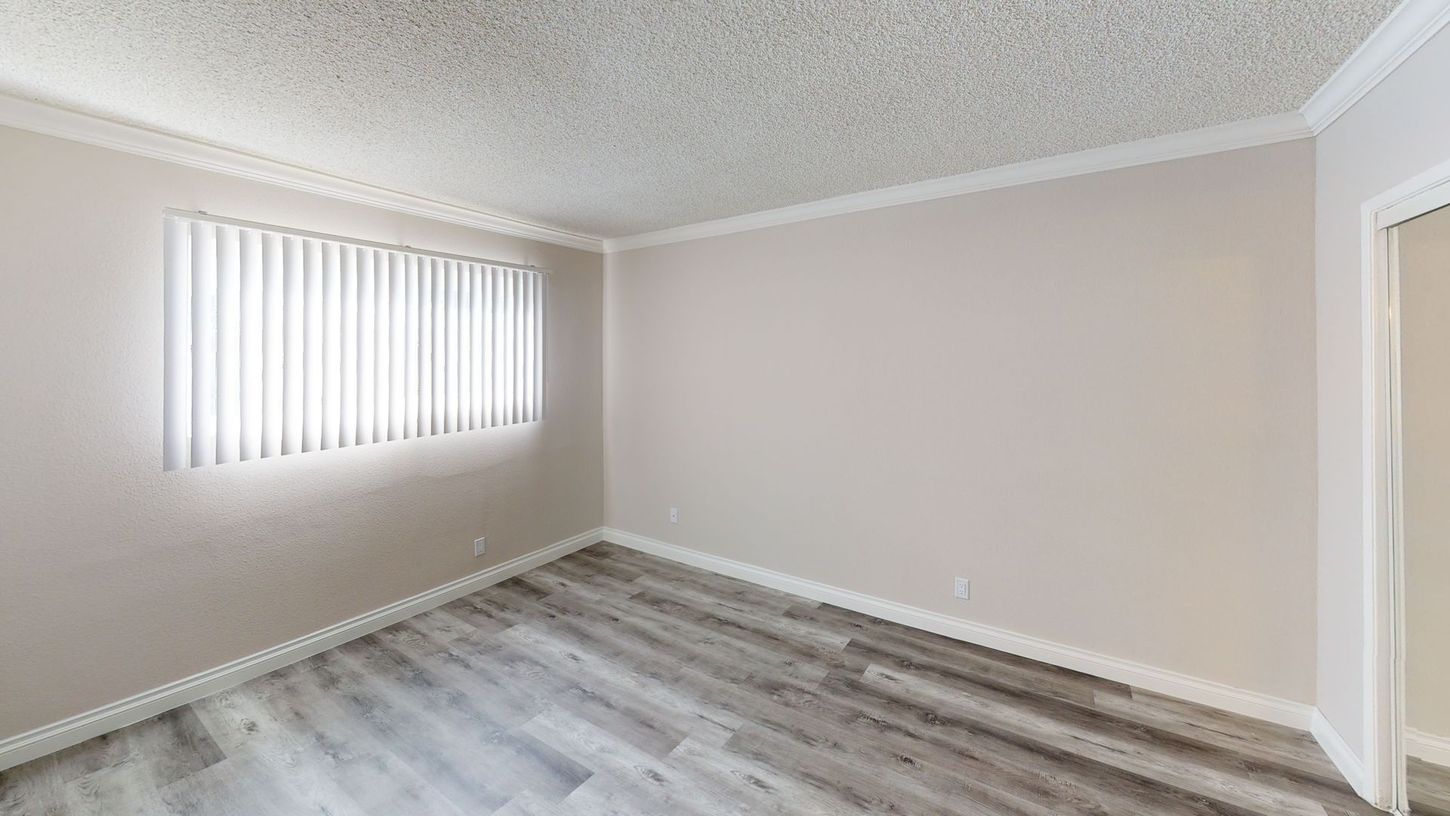 Empty room with light gray wood-look flooring, white walls, window with blinds, and a textured ceiling.