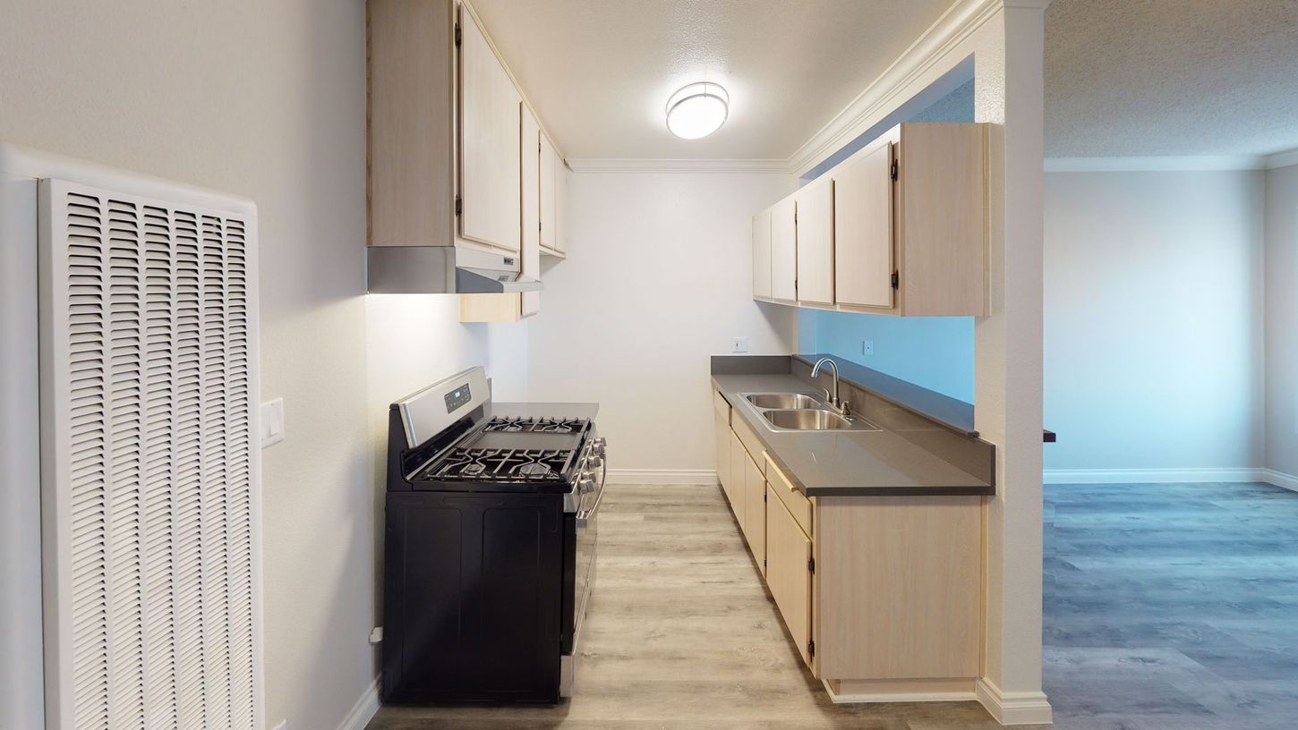 Kitchen with light wood cabinets, gray countertops, black stove, and a light fixture.