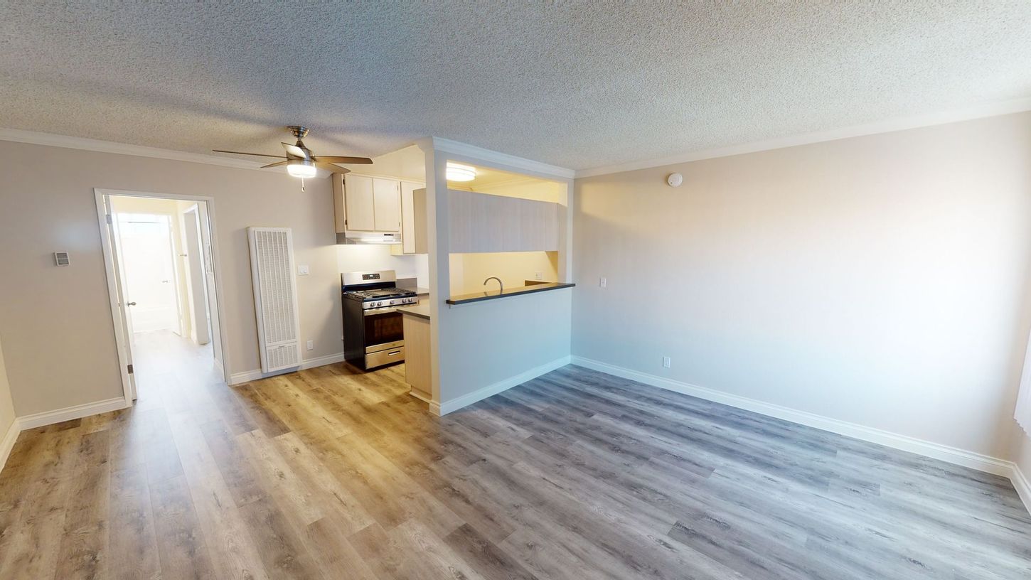 Interior of an apartment with wood-look floors, a small kitchen, and a hallway.