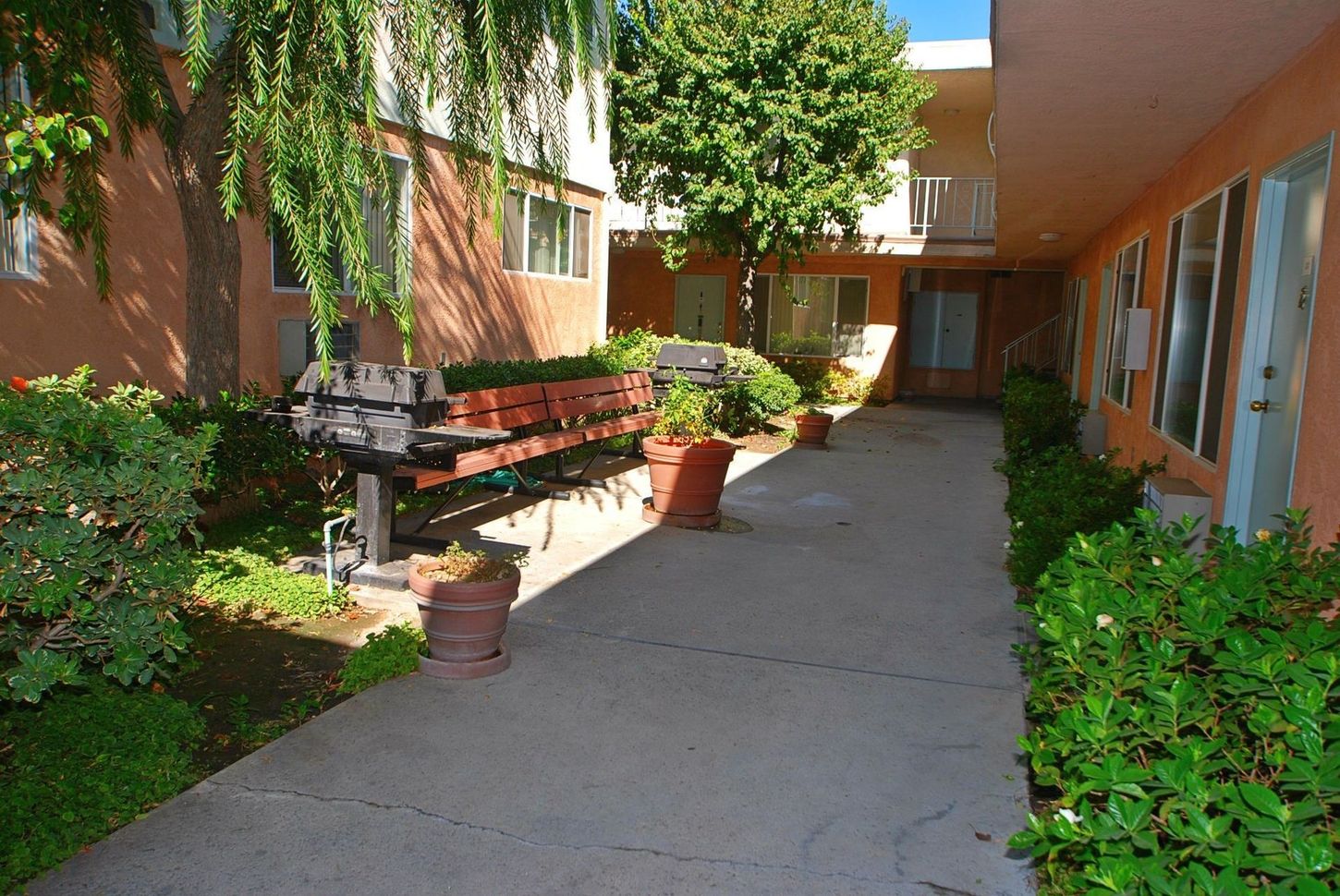 Courtyard with walkway, trees, benches, and apartment buildings with peach walls.