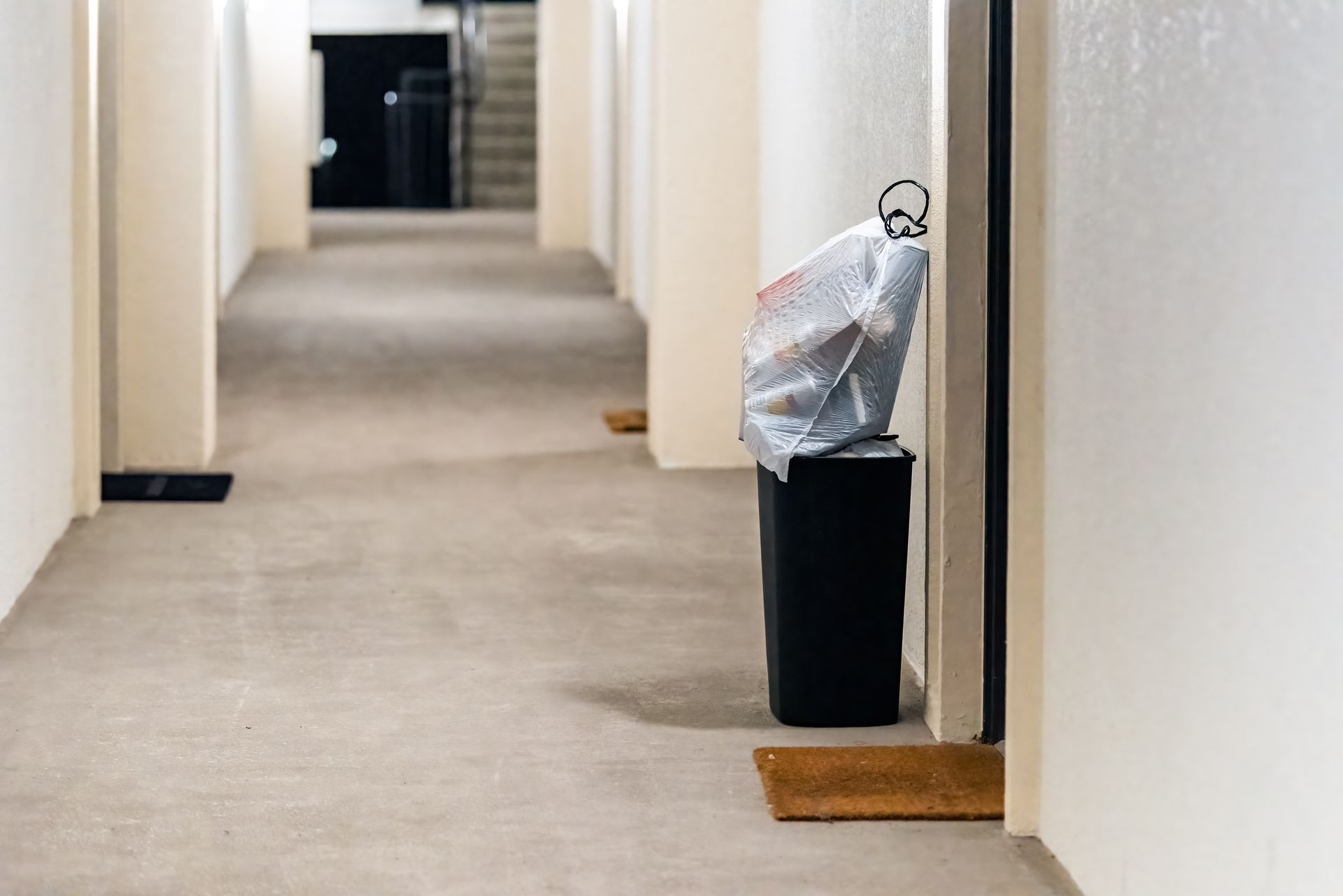 Narrow hallway with a trash bin and bag beside a doorway on the right.