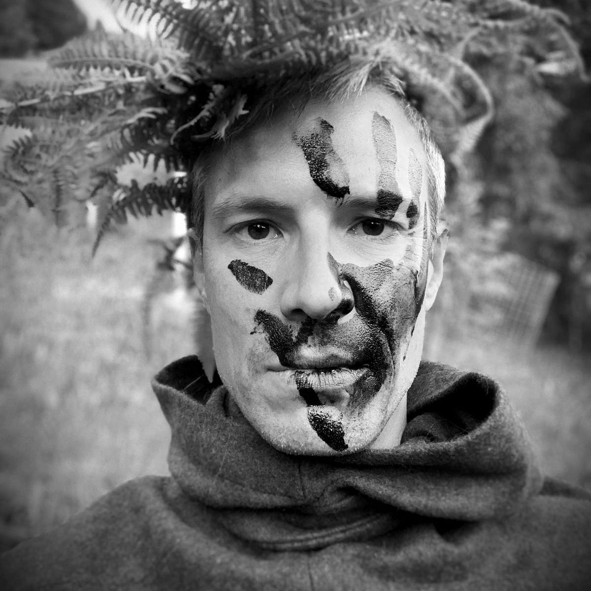 Man with brushwood on his head and handprints on his face as camouflage.
