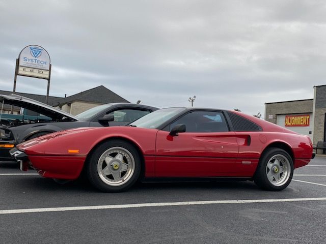 A red ferrari is parked in a parking lot next to a black car.