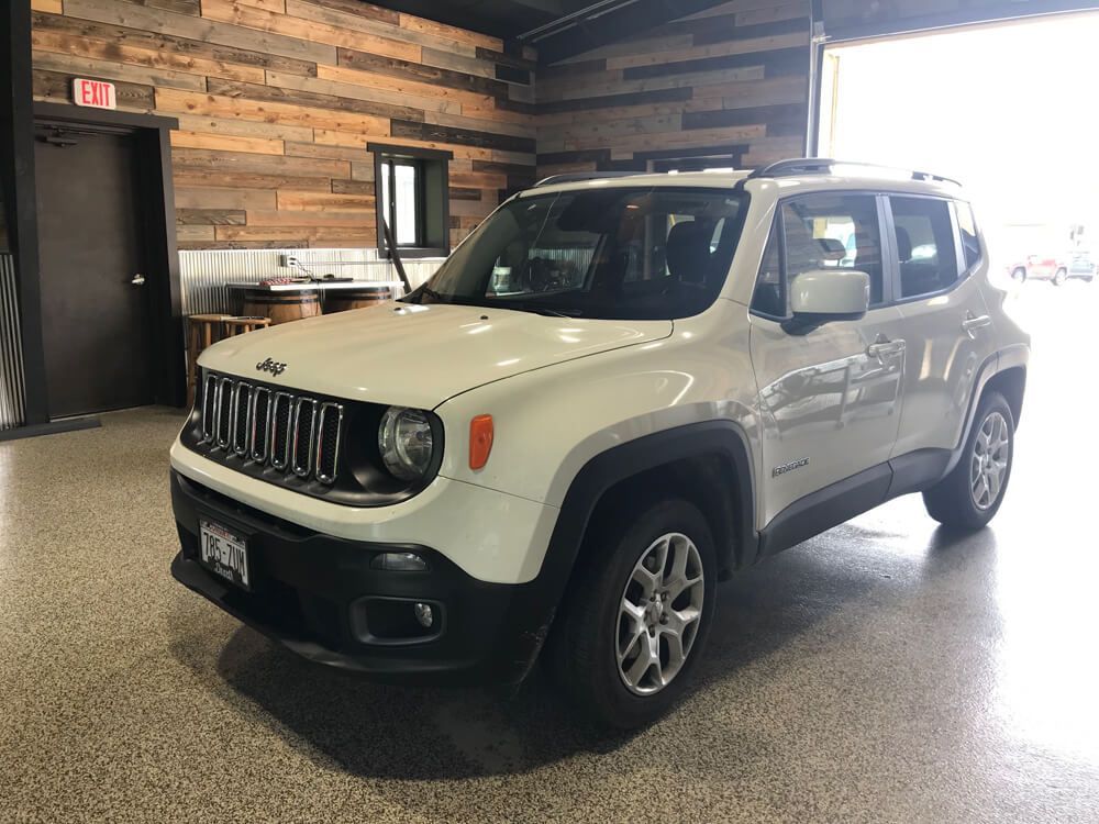 A white jeep renegade is parked in a garage.