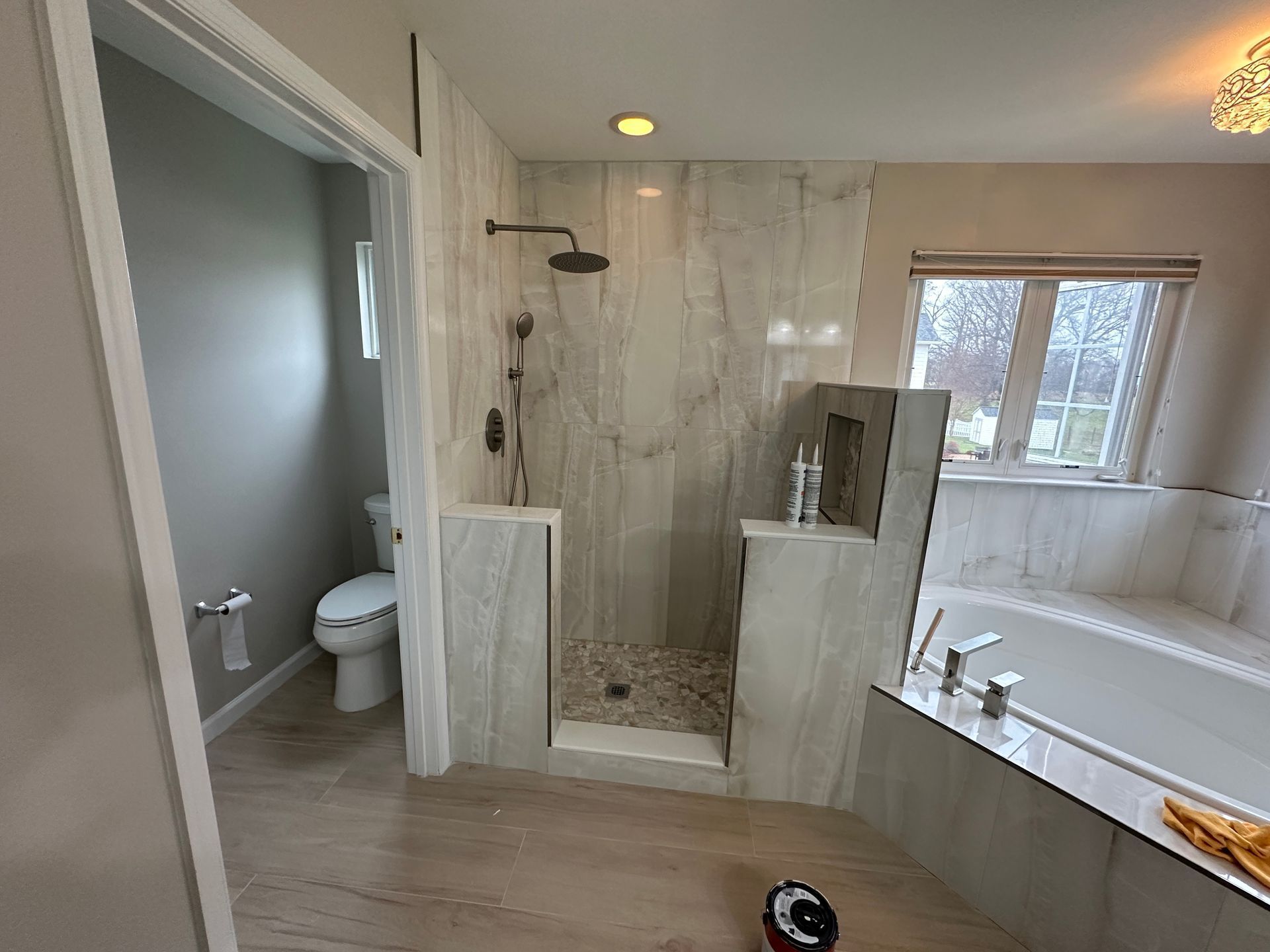 A bathroom with a walk in shower , toilet , tub and window.