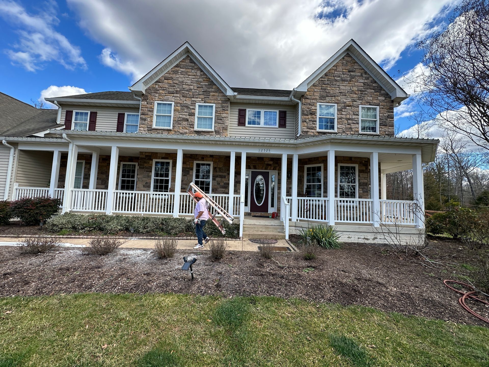 A woman is standing in front of a large house with a large porch.