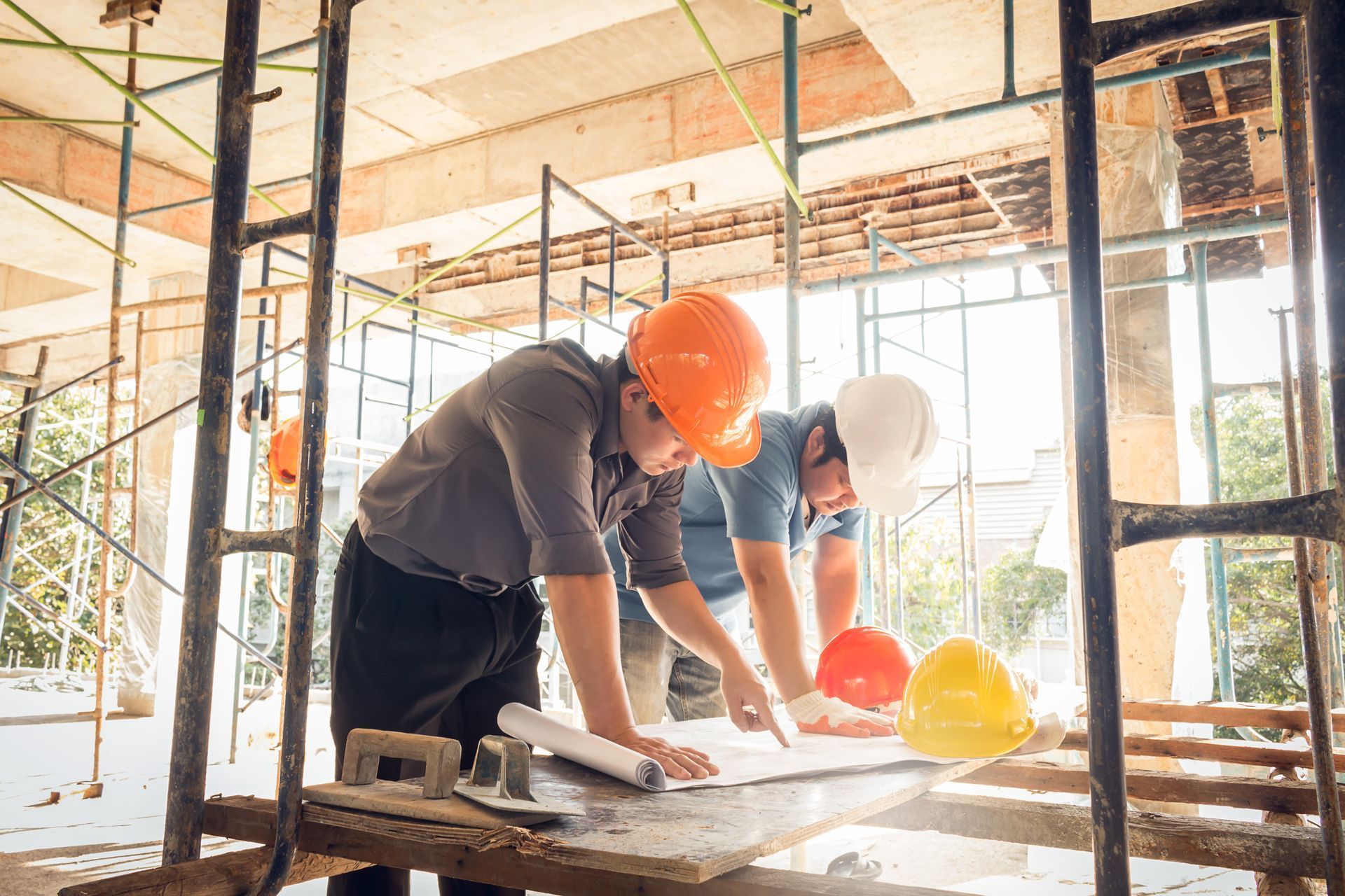 Two construction workers are looking at a blueprint at a construction site.
