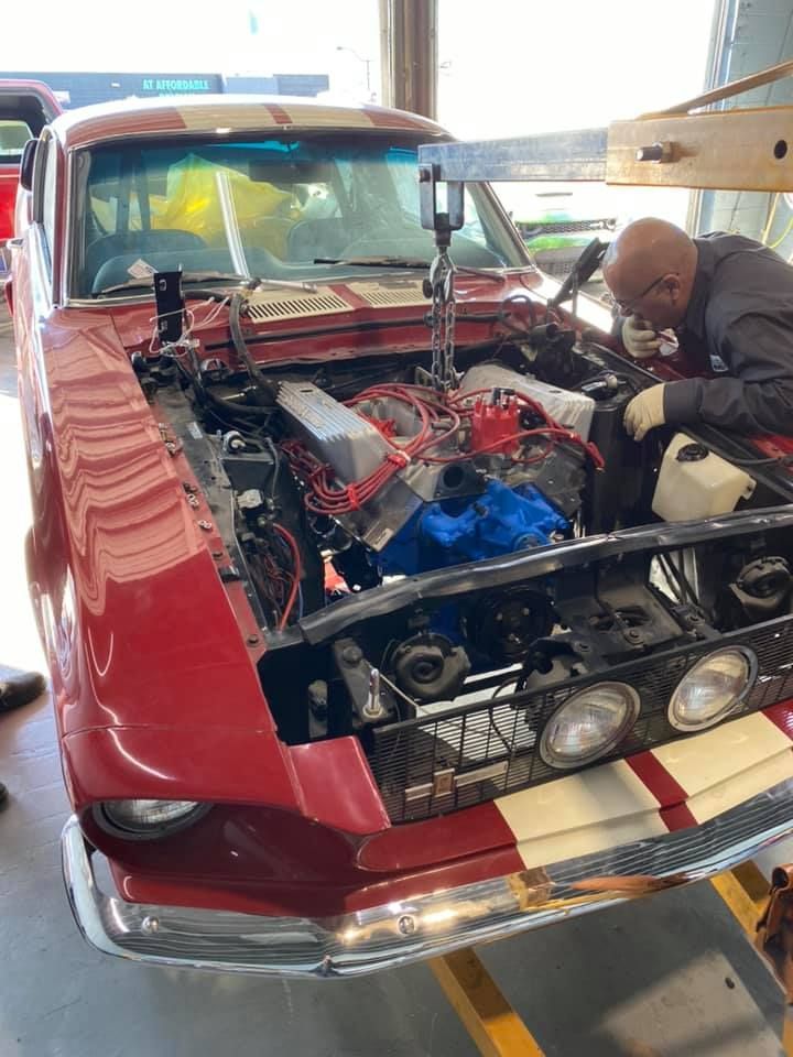 Red classic car with white stripes, engine being worked on by a mechanic.