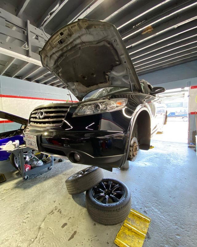 Black Infiniti FX in a repair shop with the hood open and tires off.
