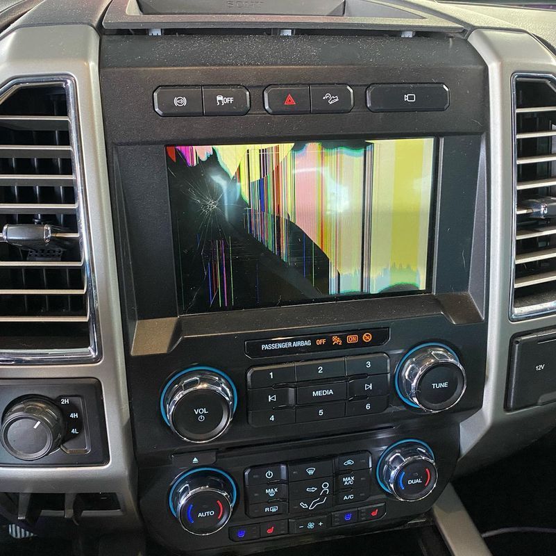 Car dashboard with a damaged infotainment screen displaying a distorted yellow and black image.