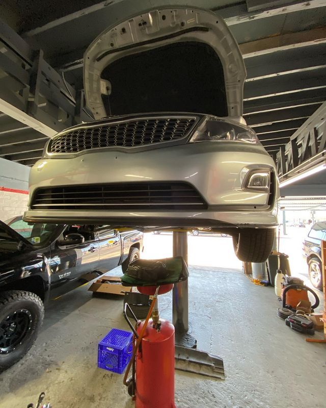 Silver car raised on a lift in a garage with hood open, preparing for repair.