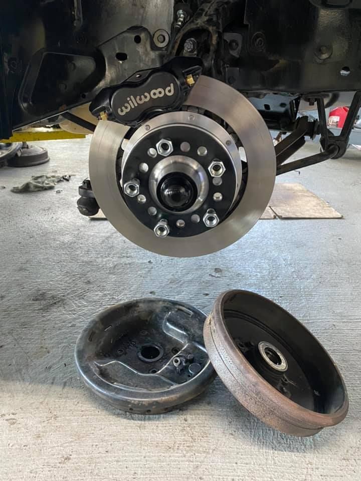 Car brake assembly showing a Wilwood disc brake, and two removed drum brake components on a concrete floor.