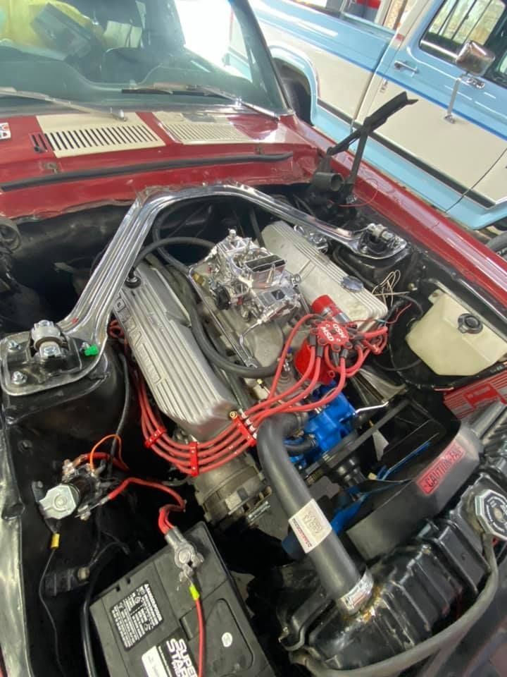 Red classic car engine bay with a modified engine, including red ignition wires, and a battery.