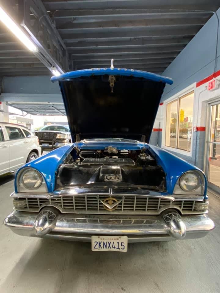 Blue classic car with hood open, in a garage.