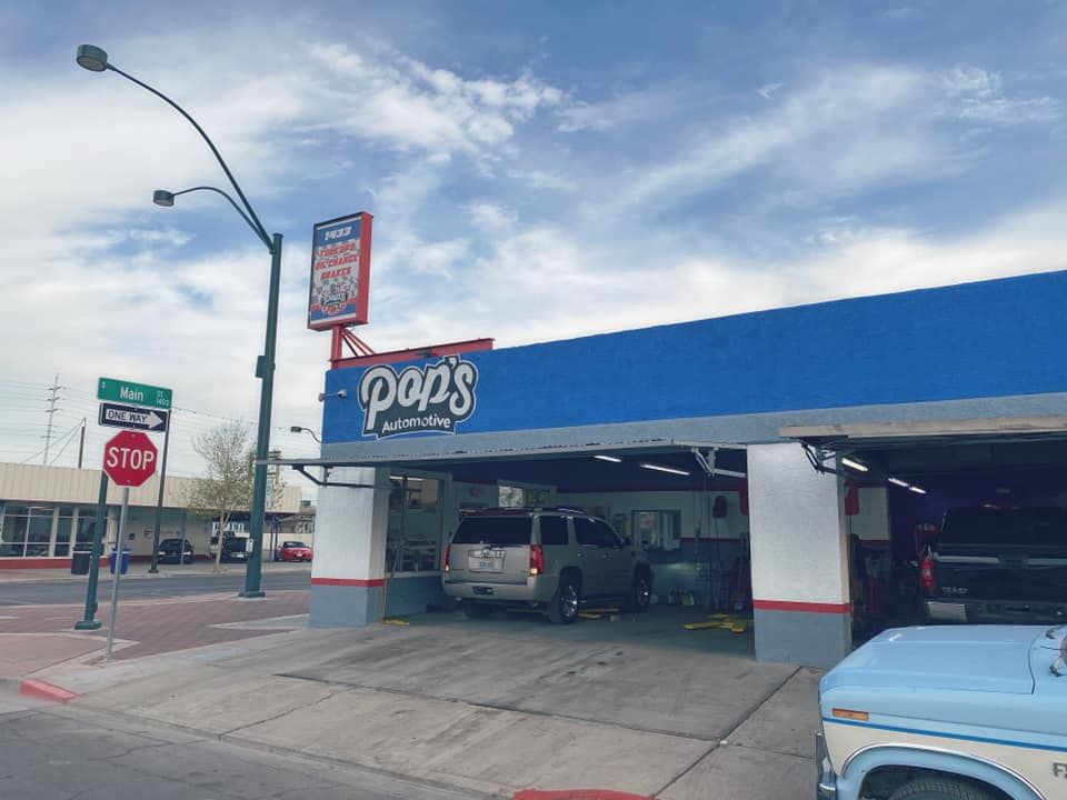 Exterior of Pop's Auto Repair shop with a blue awning and a vehicle inside the service bay under a partly cloudy sky.