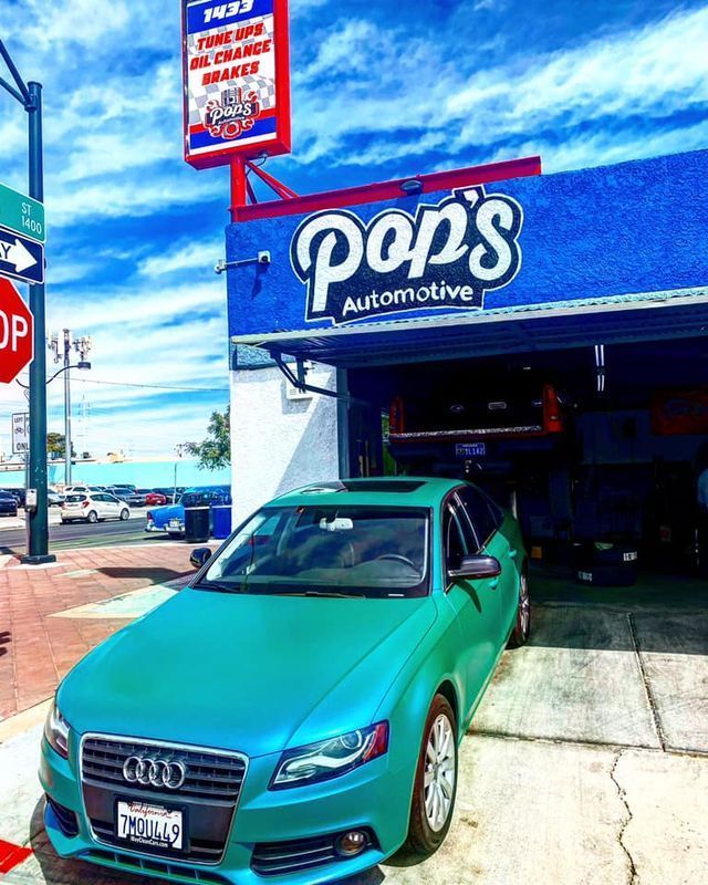 Green Audi car parked outside Pop's Automotive repair shop with a blue facade and a sign.