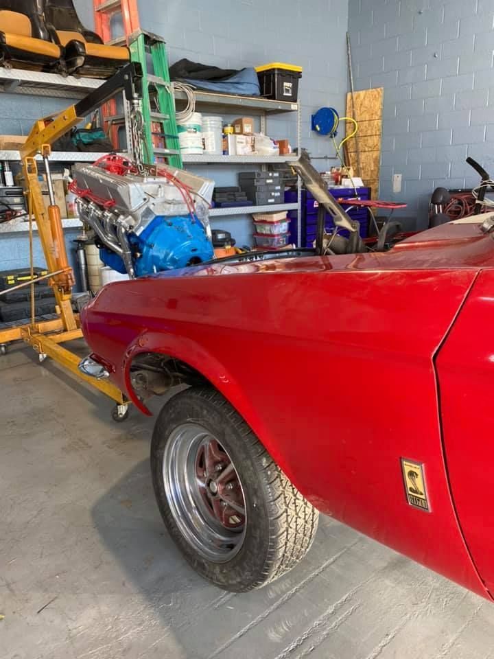 Red car with engine being lowered by a hoist in a garage.