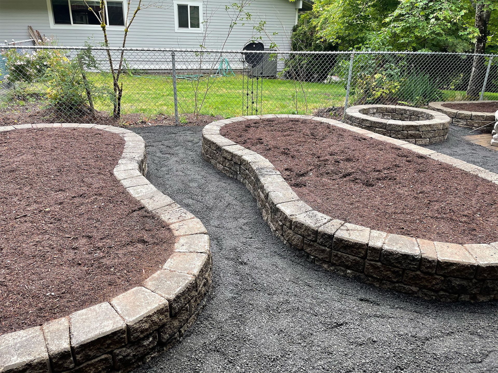A garden with a fire pit in the middle of it and a fence in the background.