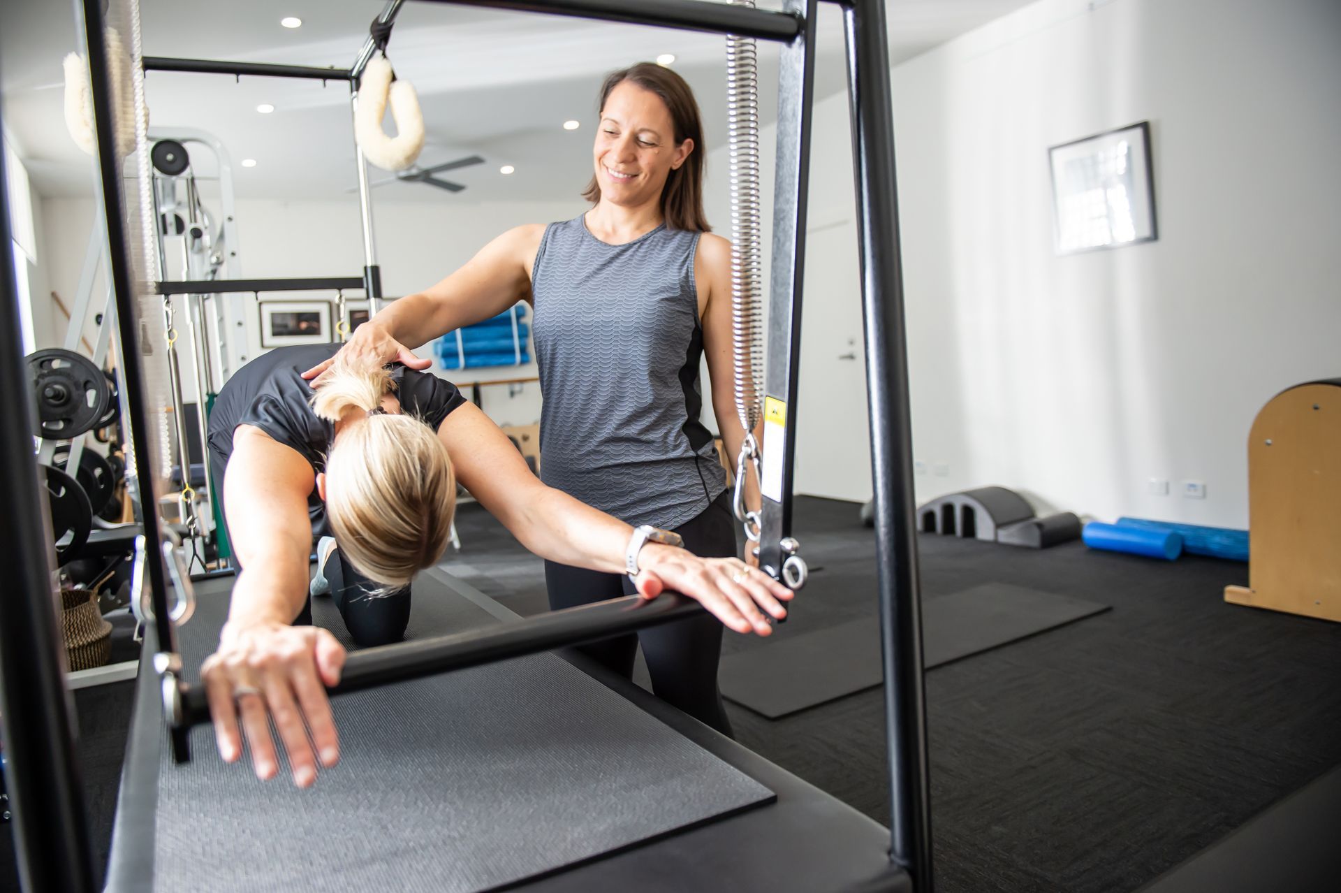 A woman is helping another woman do a pilates exercise in a gym.