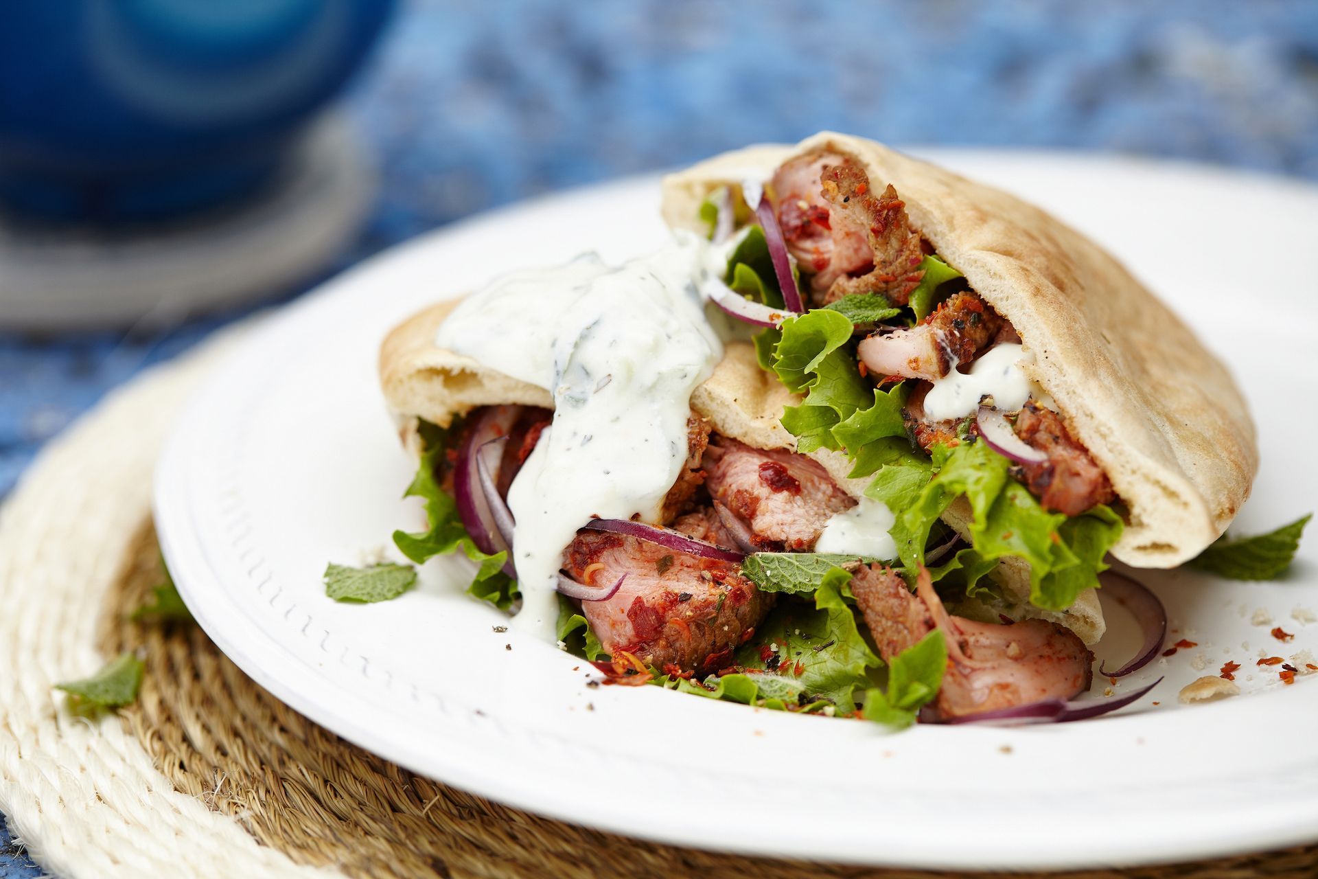 A pita sandwich with meat and lettuce on a white plate.