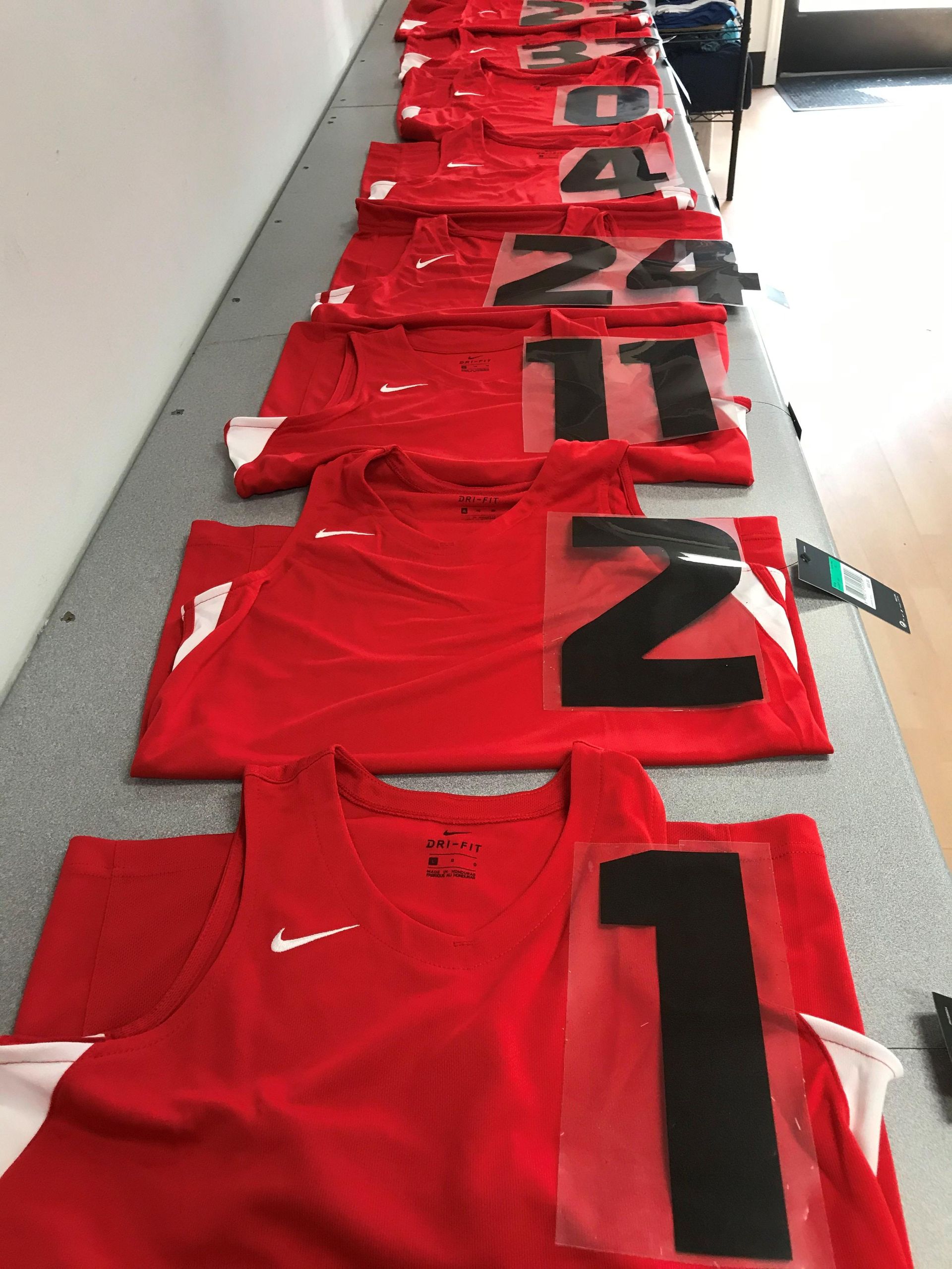 A row of red nike tank tops with black numbers on them