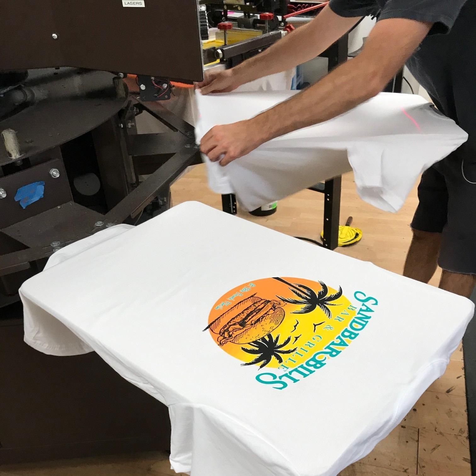 A man is printing a shirt that says sandbar grills