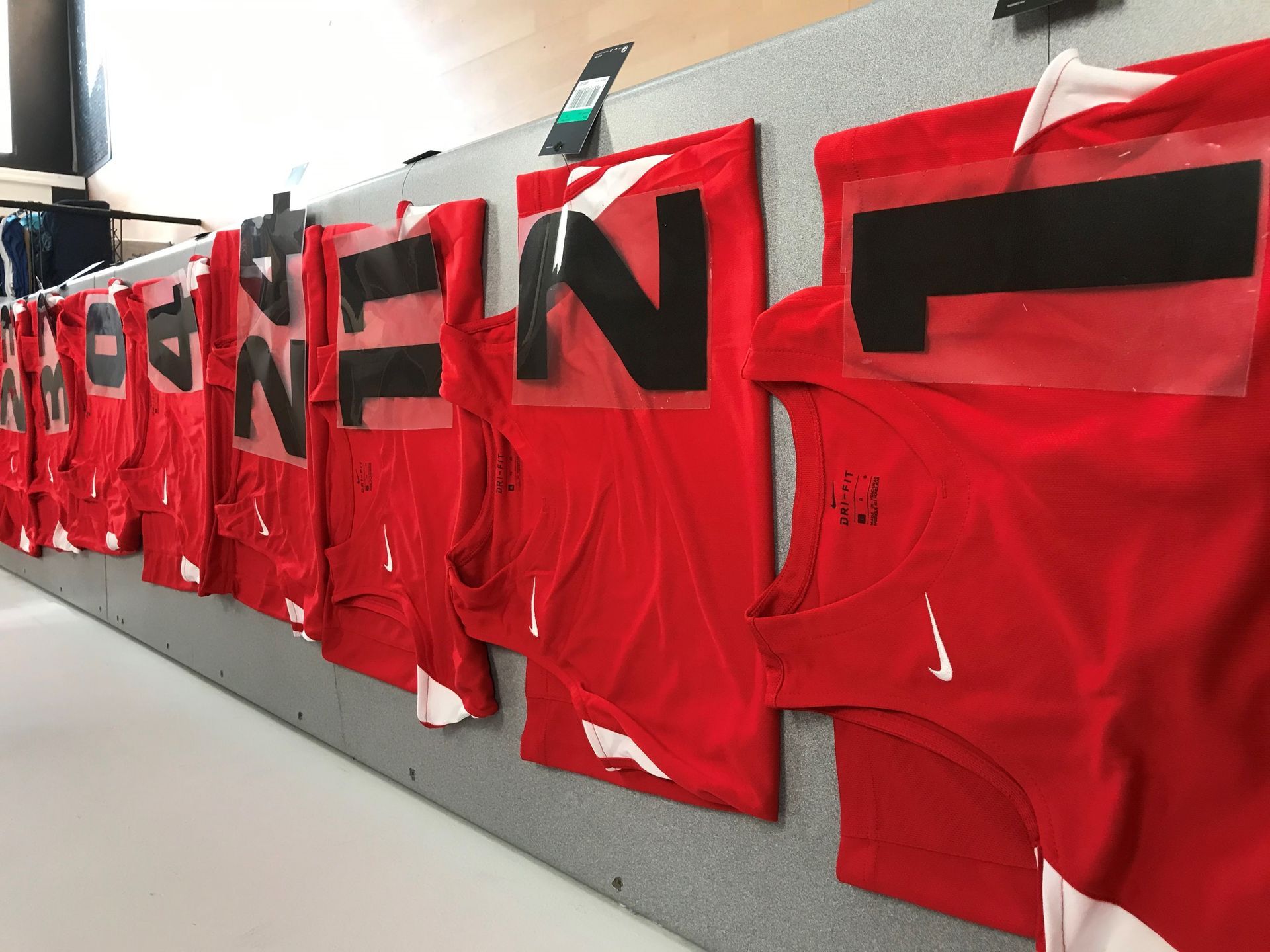 A row of red nike jerseys are hanging on a wall.