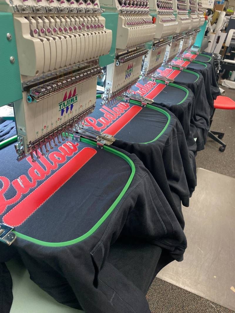 A row of shirts are being embroidered on a machine.