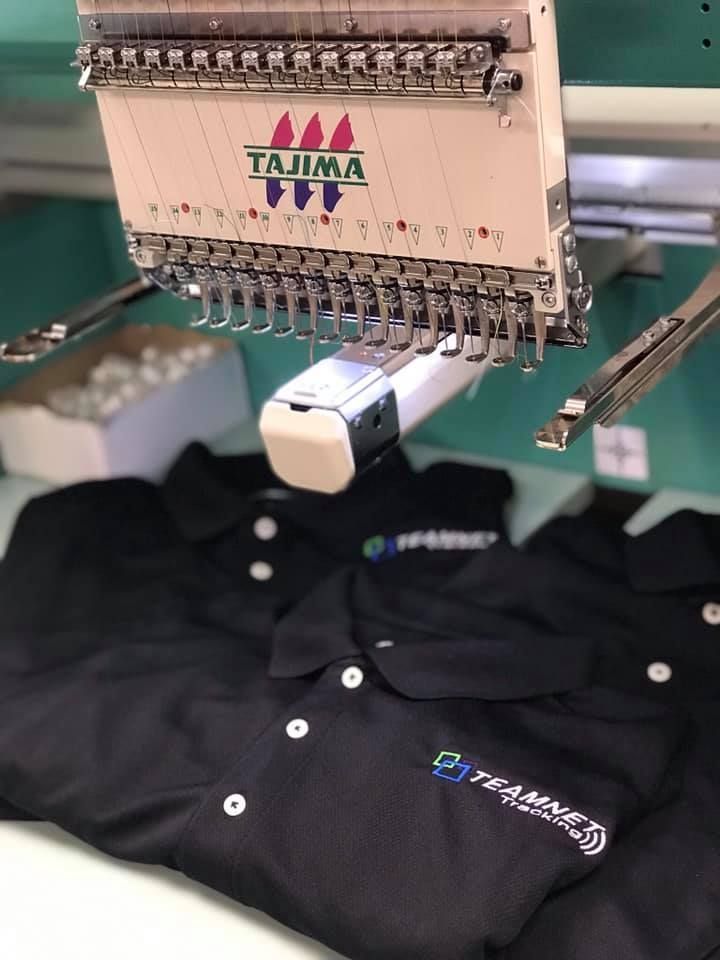 A black polo shirt is being embroidered on a machine.