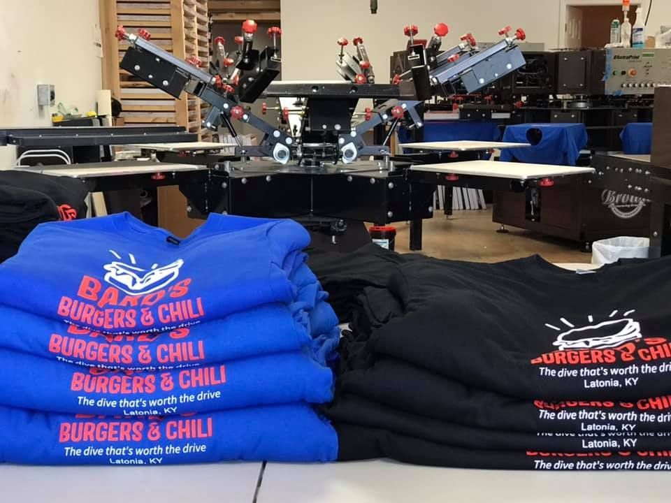 A stack of blue and black shirts that say burgers & chili